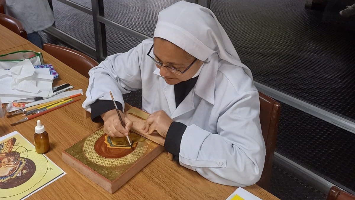 Ir. Plácida Santos, OSB, curvada sobre a mesa de trabalho, pinta um ícone com pincel fino